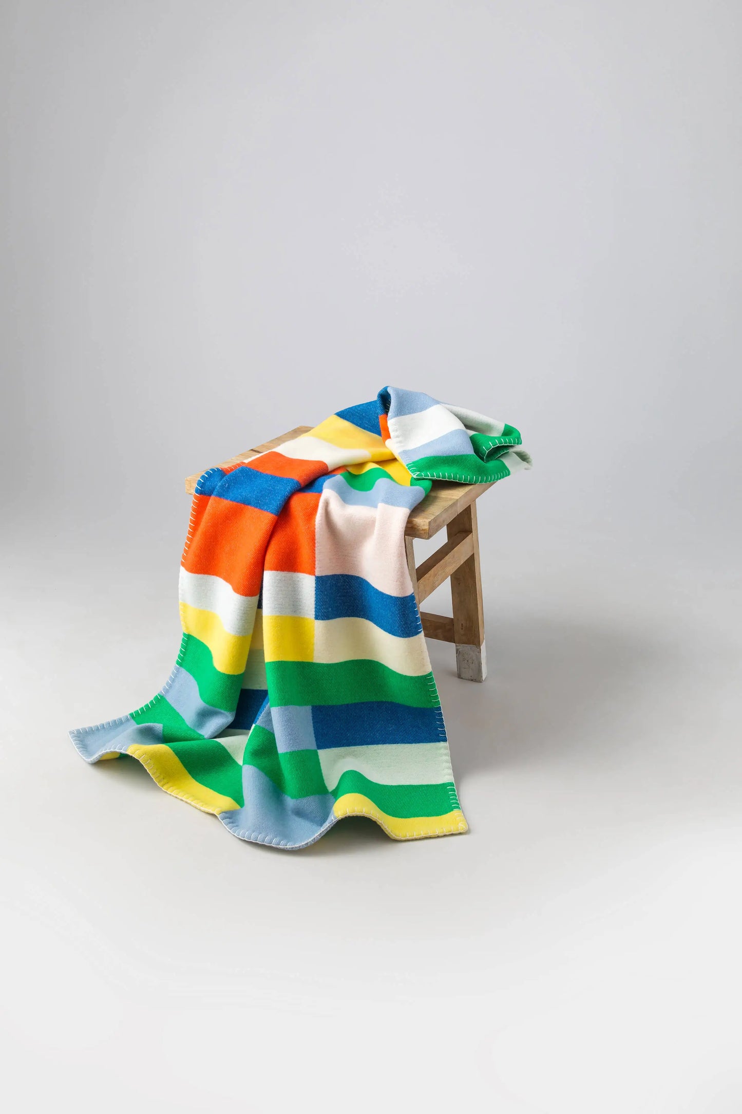 2025 Johnstons of Elgin Interiors Collection  Block Stripe' Children's Blanket draped over a wooden stool on a grey background  TB000582RU7439ONE