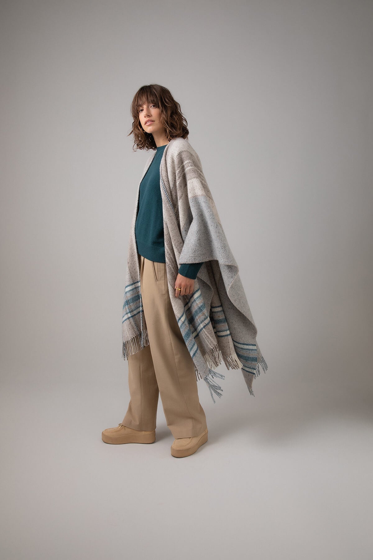 Side of Johnstons of Elgin Cashmere Wool Blend Textured Donegal Cape Natural Multi worn over an Mallard Cashmere Sweater and Camel Trousers on a grey background TB000632RU7370ONE