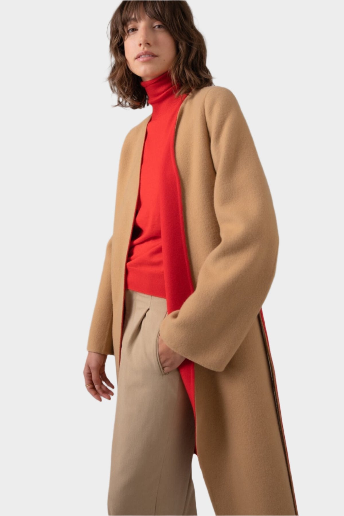 Model wearing Johnstons of Elgin Women's Collarless Cape Wool Blend Coat in Camel & Red worn with a matching Roll Neck Sweater and Camel Trousers on a grey background TB000633RU7380