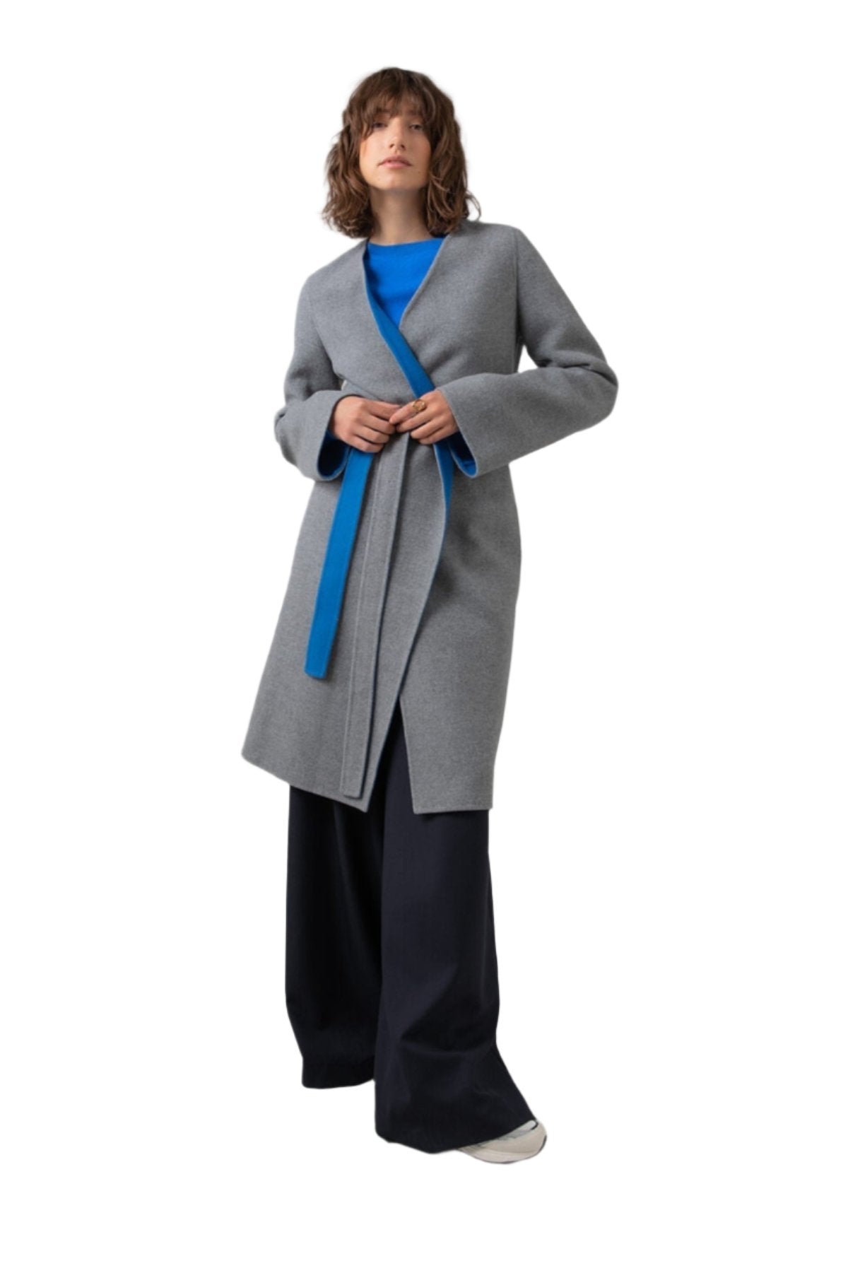 Johnstons of Elgin Women's Collarless Cape Wool Blend Coat in Mid Grey & Blue worn with an Orkney Blue Sweater and Navy Trousers on a grey background TB000633RU7381