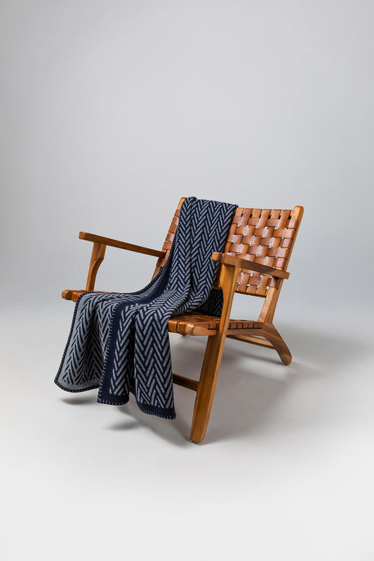 Johnstons of Elgin’s Navy & Mid Grey Herringbone Blanket Stitch Throw on brown chair on a grey background TB000500RU6974ONE