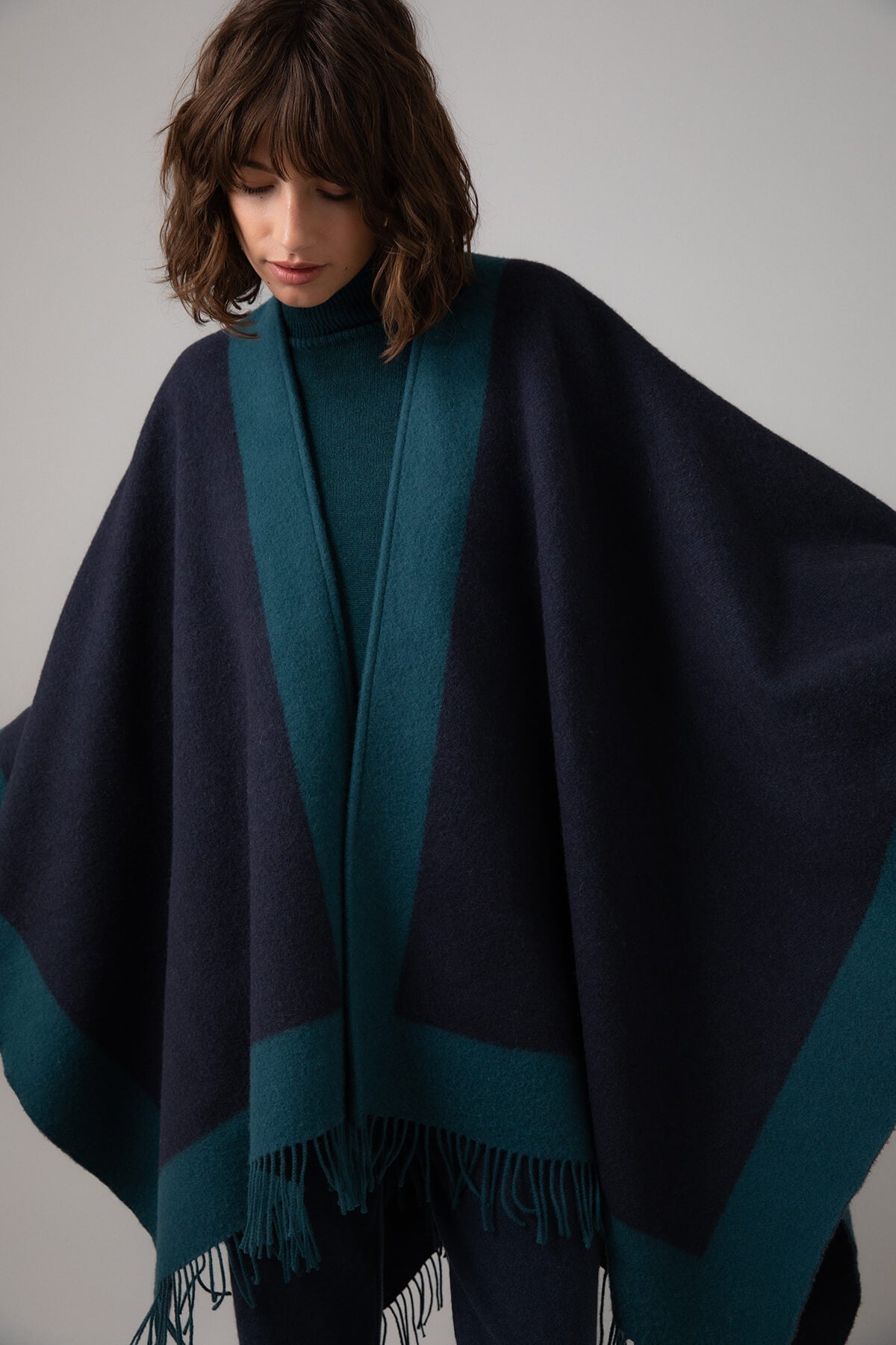 Model wearing Johnstons of Elgin Merino Wool Cape with Contrast Border in Mallard worn matching sweater and Mazarine Joggers on a grey background TD000230RU7358ONE