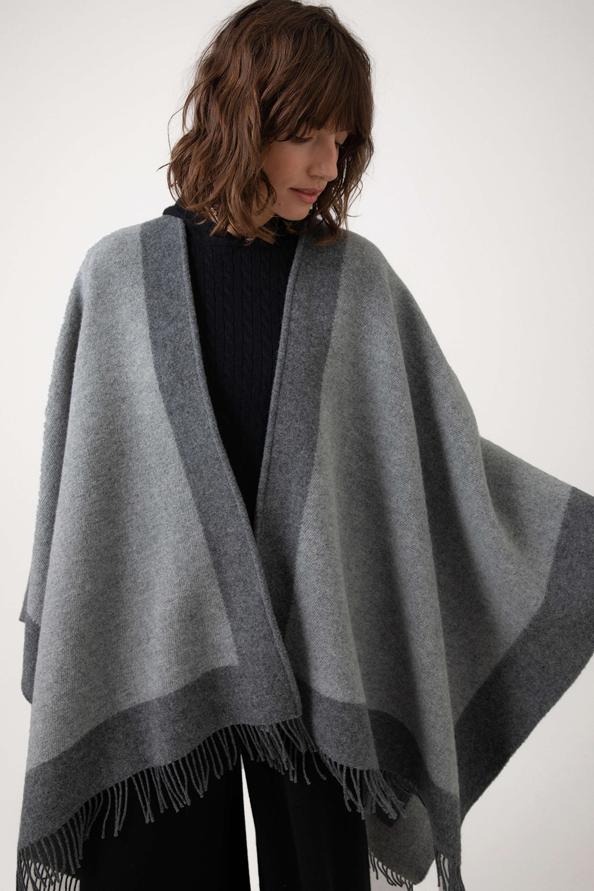 Model wearing Johnstons of Elgin Merino Wool Cape with Contrast Border in Grey worn over Navy hoodie & Joggers on a grey background TD000230RU7369ONE