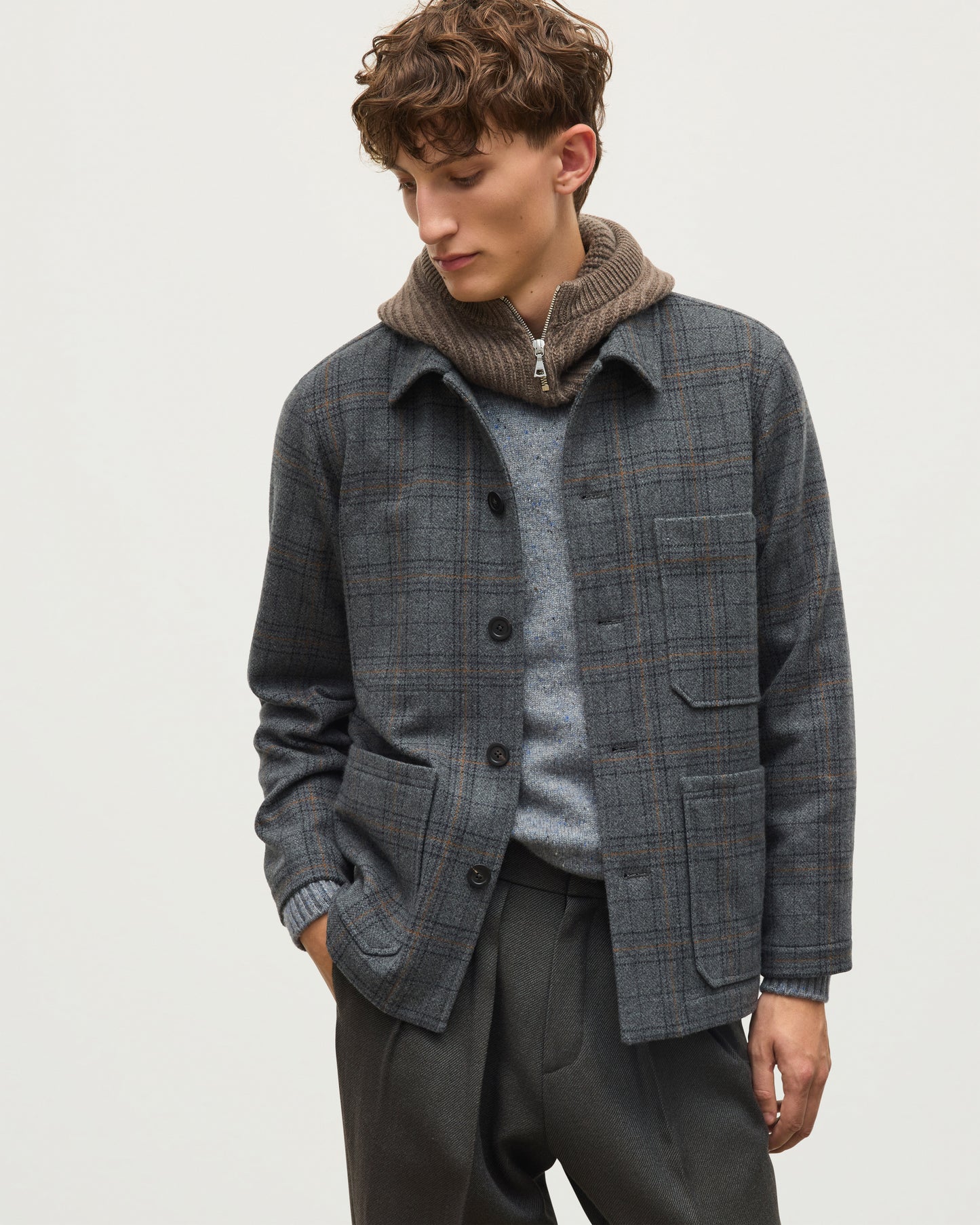 A man wearing a gray and brown plaid overshirt over a gray knit sweater and a brown ribbed knit neck warmer, paired with dark gray trousers, against a light gray studio background. JOHNSTONS OF ELGIN MENS WOOL WEAVERS JACKET 100% WOOL AND NEVIS CASHMERE SNOOD TD000546RU7862