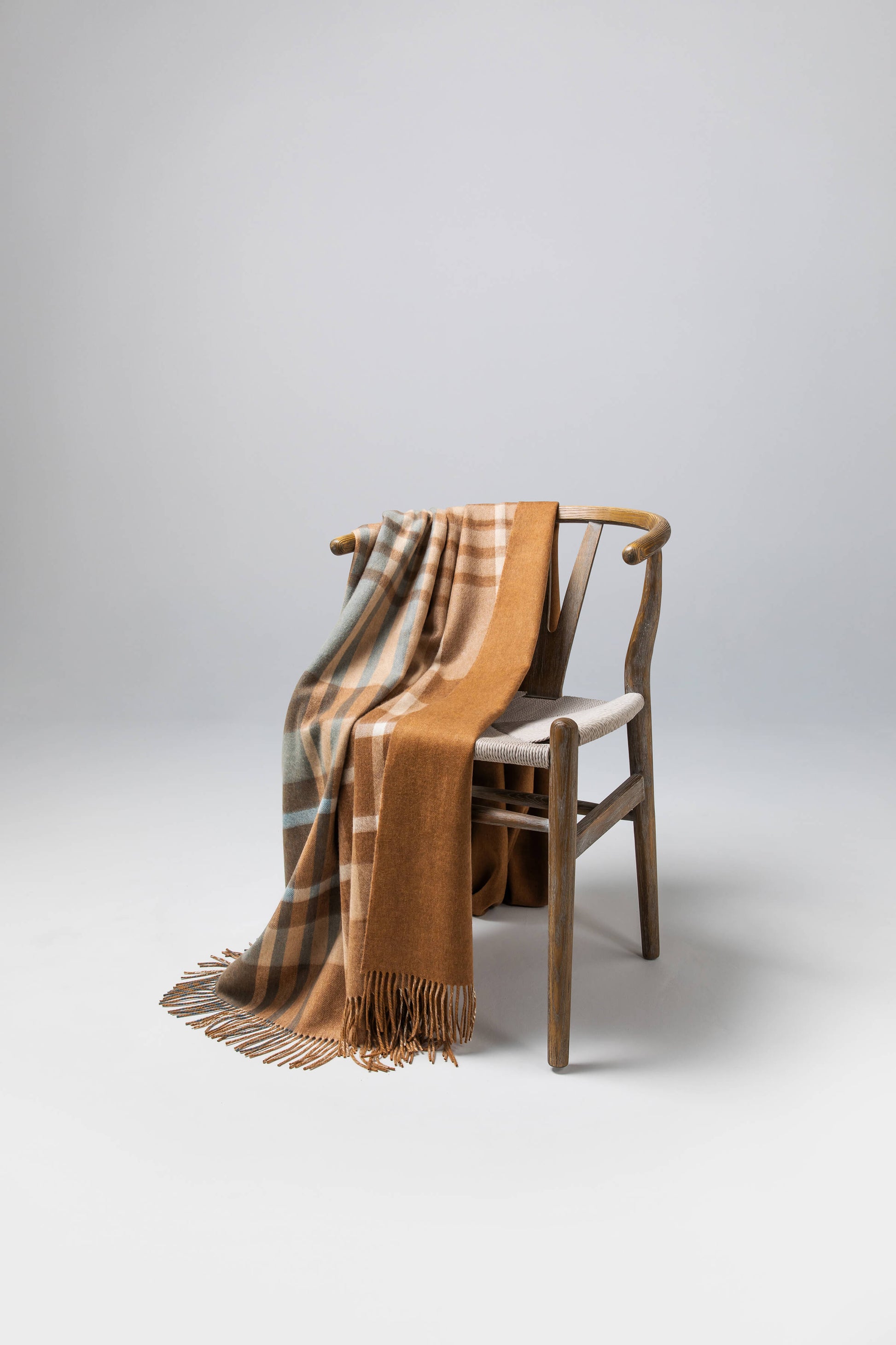 Johnstons of Elgin’s Connon Check Reversible Cashmere Throw on brown chair on a grey background WA000013RU7285