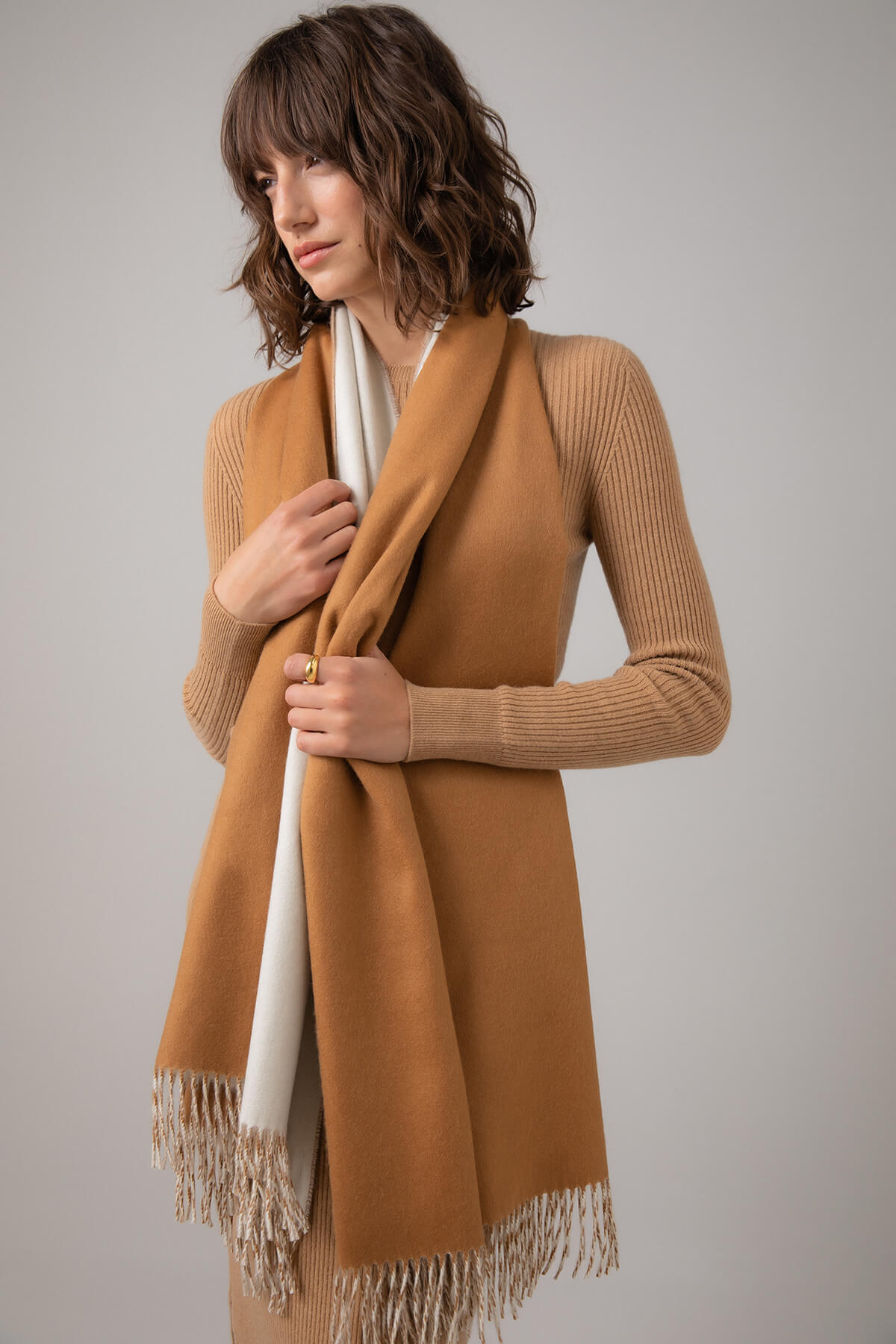 Model wearing a Johnstons of Elgin Reversible Cashmere Stole in Dark Camel over a Camel Cashmere Sweater on a grey background WA000585RU5244ONE