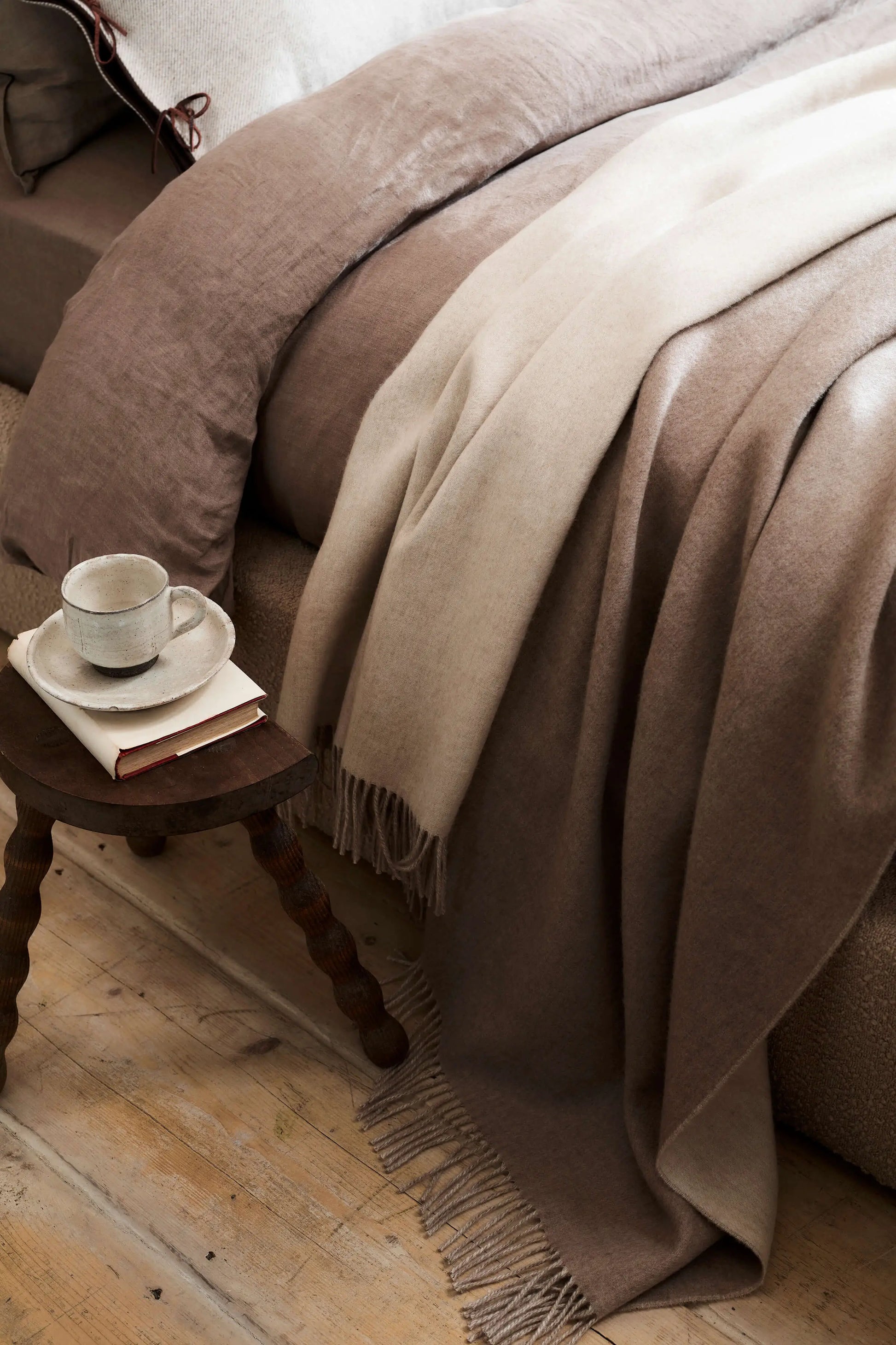 Johnstons of Elgin Blanket Collection Light Brown & Light Grey Reversible Cashmere Bed Throw on a bed with a teacup and book on a bedside table WA001374RU6323ONE