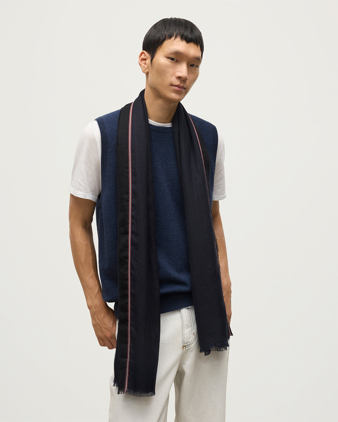 MALE MODEL WEARS IVES CHEVRON BORDER SCARF NAVY 100% CASHMERE OVER A NAVY SLEEVELESS CASHMERE SWEATER, WITH WHITE T-SHIRT AND JEANS  WA002446RU7699ONE