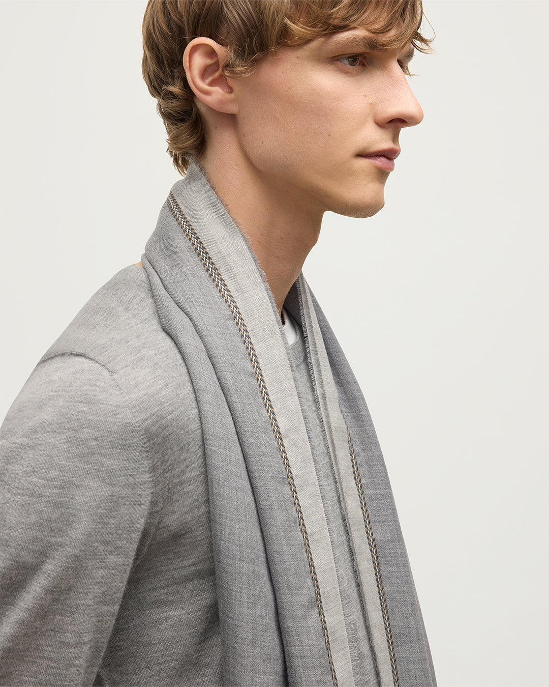MALE MODEL WEARS JOHNSTON OF ELGIN IVES CHEVRON BORDER SCARF 100% CASHMERE OVER A GREY SUPERFINE CASHMERE SWEATER WA002446RU7700ONE