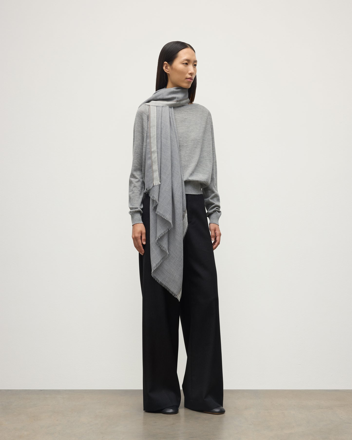 MODEL WEARS JOHNSTON OF ELGIN IVES CHEVRON BORDER SCARF 100% CASHMERE OVER A LIGHT GREY CASHMERE SWEATER WA002446RU7700ONE