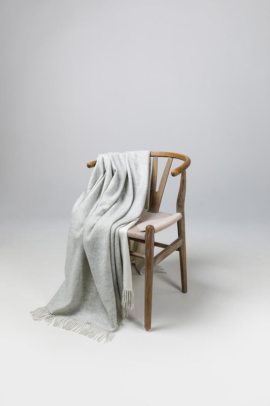 Johnstons of Elgin Reversible Pure Cashmere Throw in Silver & White draped over a wooden chair on a white background WA000013RU5059ONE