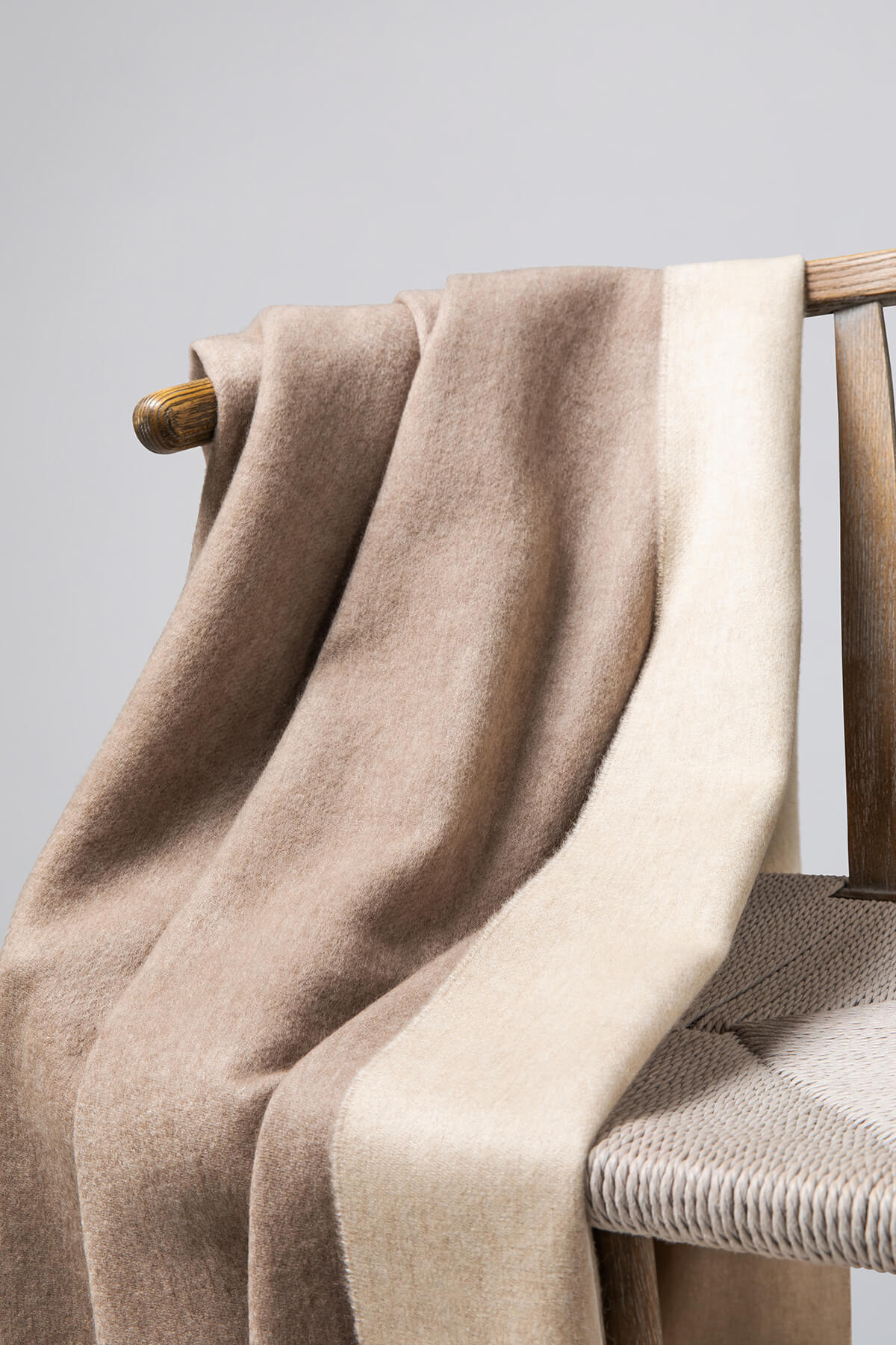 Detail of Johnstons of Elgin Reversible Pure Cashmere Throw in Light Brown & Light Grey draped over a wooden chair on a white background WA000013RU5594ONE