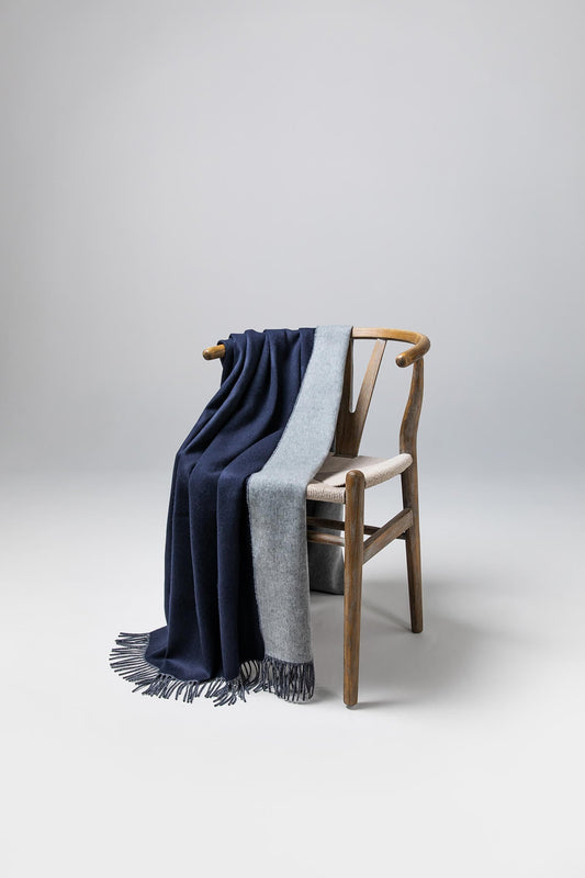 Johnstons of Elgin Reversible Pure Cashmere Throw in Navy & Light Grey draped over a wooden chair on a white background WA000013RU6632ONE