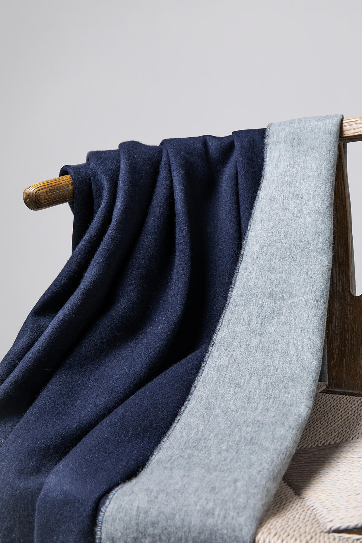 Close up of Johnstons of Elgin Reversible Pure Cashmere Throw in Navy & Light Grey draped over a wooden chair on a white background WA000013RU6632ONE