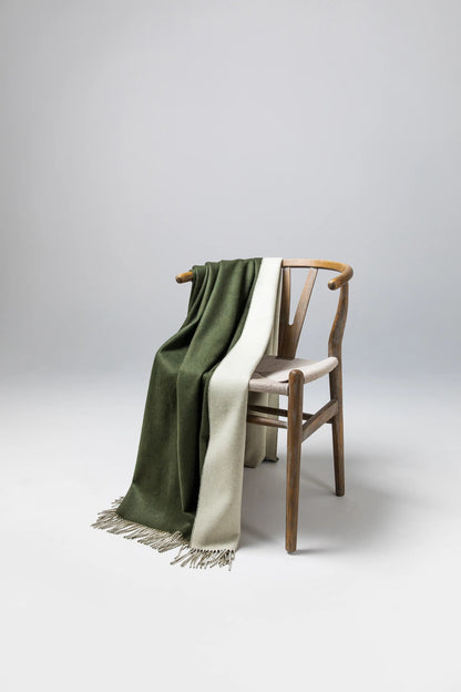 Details of Johnstons of Elgin Reversible Pure Cashmere Throw in Forest Green & Pale Olivine draped over a wooden chair on a grey background WA000013RU7255ONE