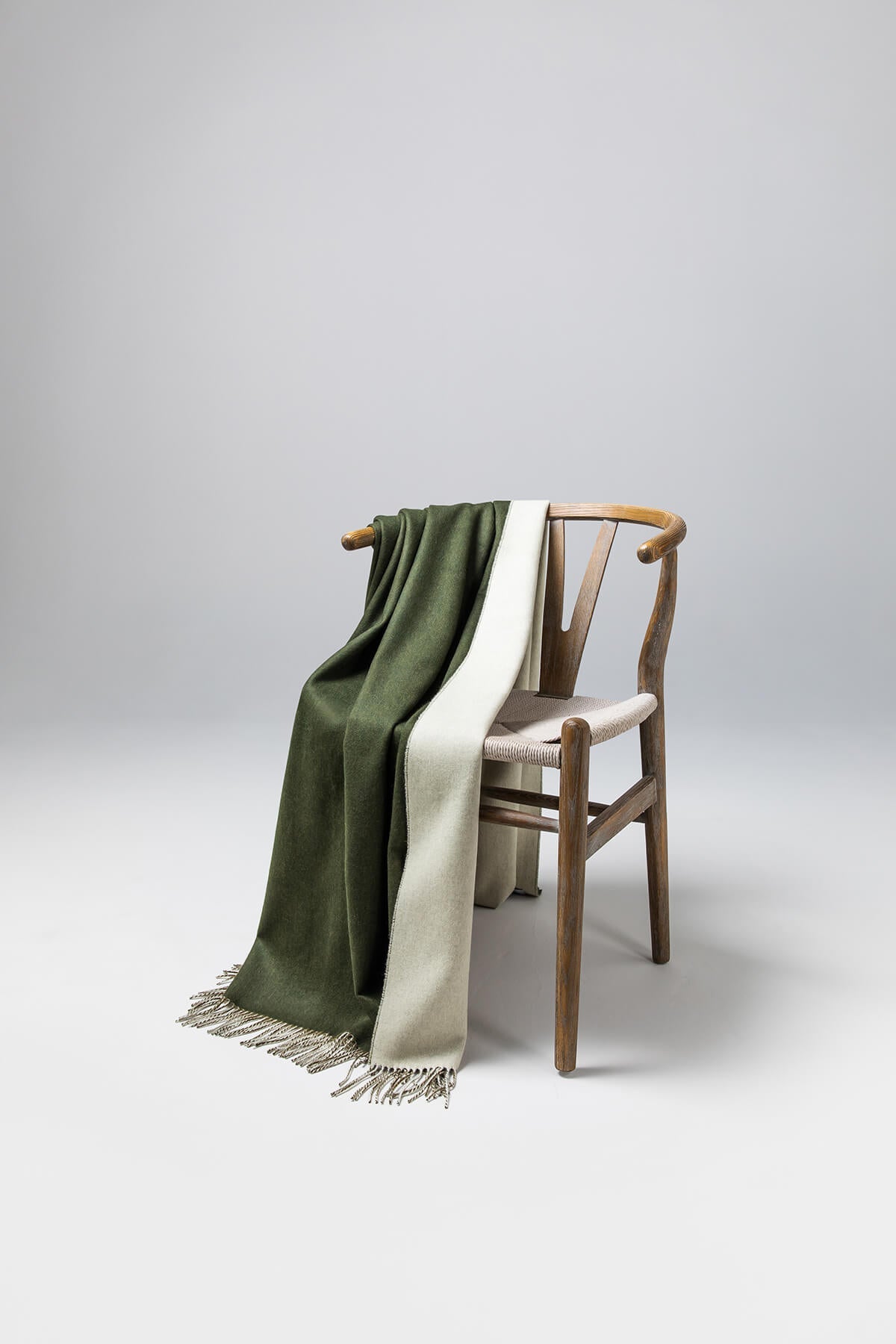 Johnstons of Elgin Reversible Pure Cashmere Throw in Forest Green & Pale Olivine draped over a wooden chair on a white background WA000013RU7255ONE