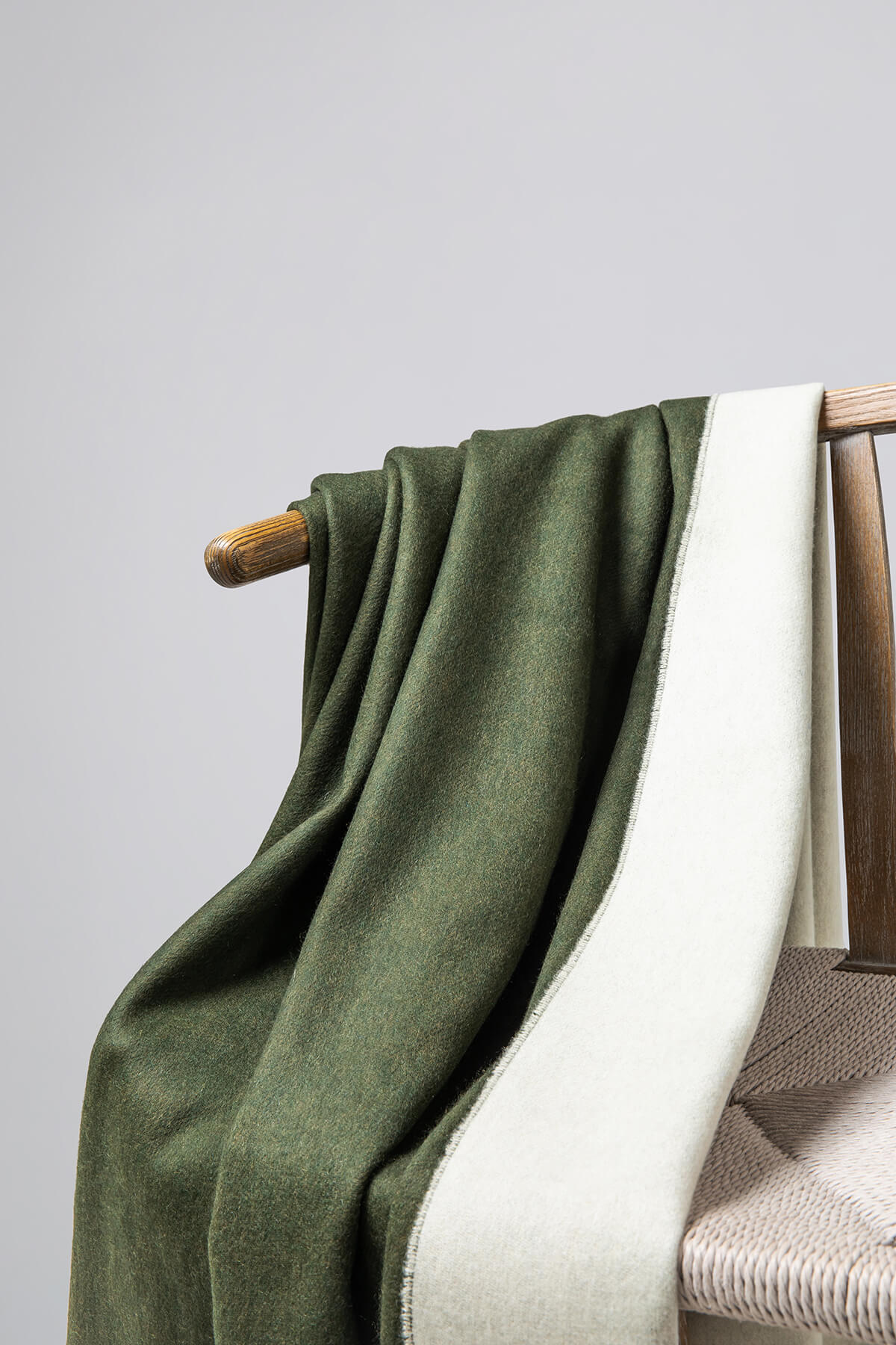 Details of Johnstons of Elgin Reversible Pure Cashmere Throw in Forest Green & Pale Olivine draped over a wooden chair on a white background WA000013RU7255ONE