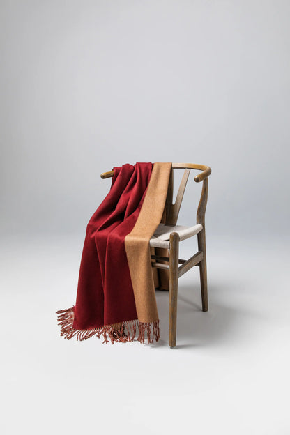 Johnstons of Elgin Reversible Pure Cashmere Throw in Claret & Fawn draped over a wooden chair on a grey background WA000013RU7256ONE