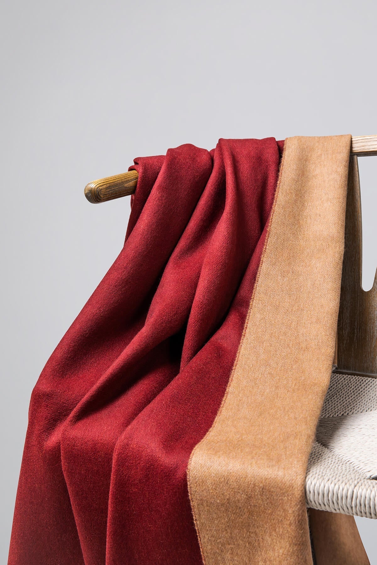 Detail of Johnstons of Elgin Reversible Pure Cashmere Throw in Claret & Fawn draped over a wooden chair on a white background WA000013RU7256ONE