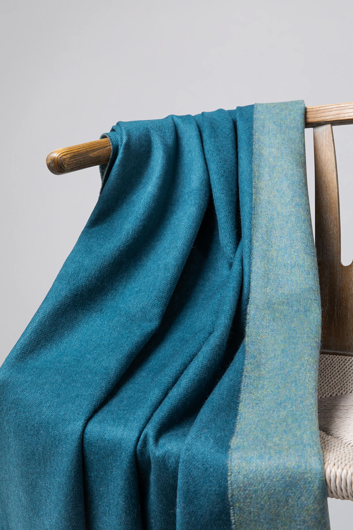 Details of Johnstons of Elgin Reversible Pure Cashmere Throw in Teal & Lovat draped over a wooden chair on a white background WA000013RU7257ONE
