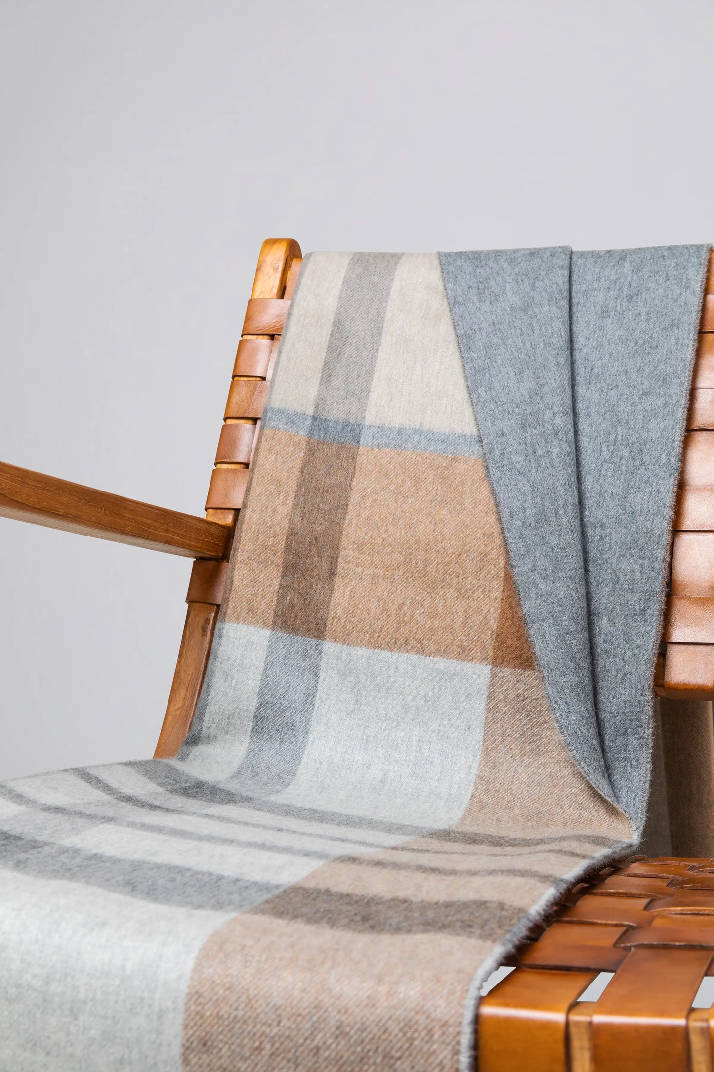 Johnstons of Elgin’s Leven Check Reversible Cashmere Throw on brown chair on a grey background WA000013RU7288ONE