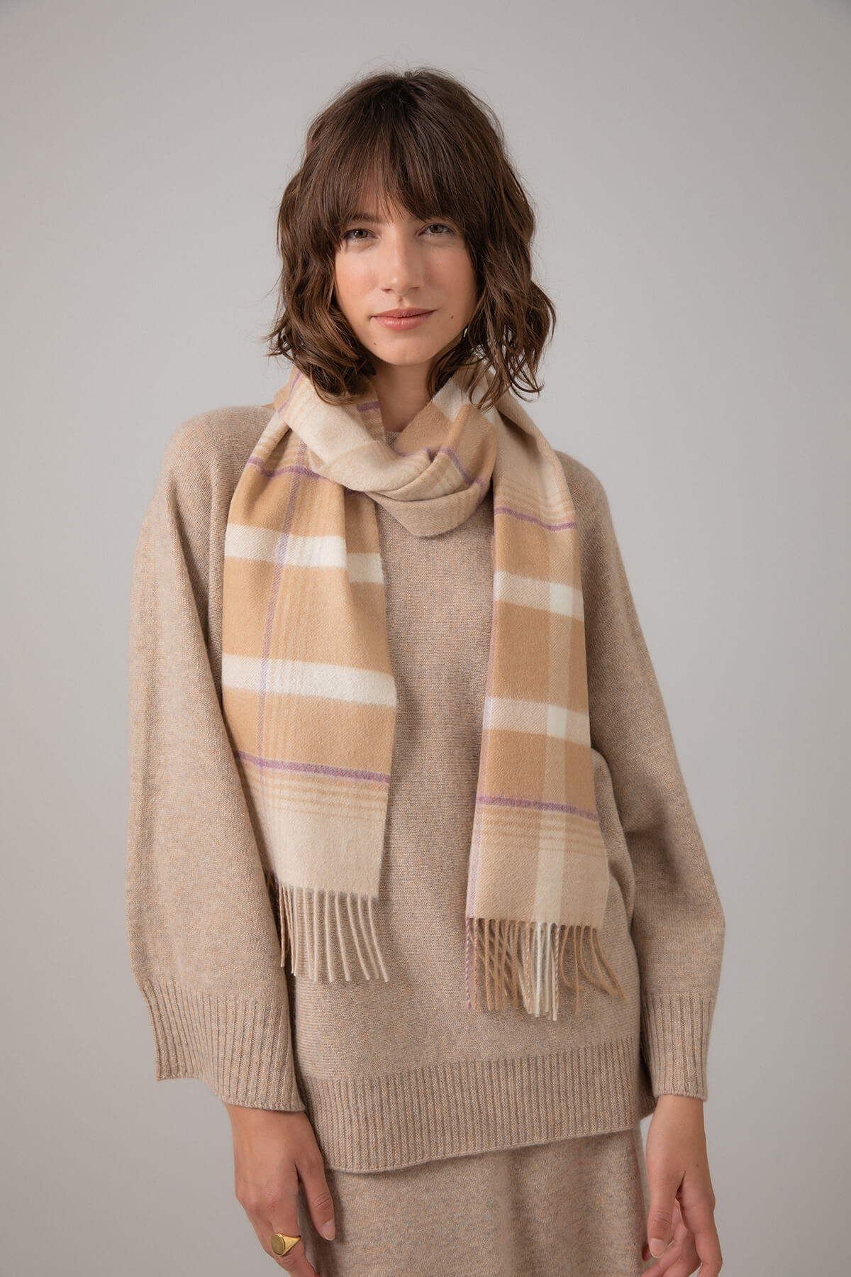 Model wearing Johnstons of Elgin Asymmetric Check Cashmere Scarf in Camel on a grey background WA000016RU7317ONE