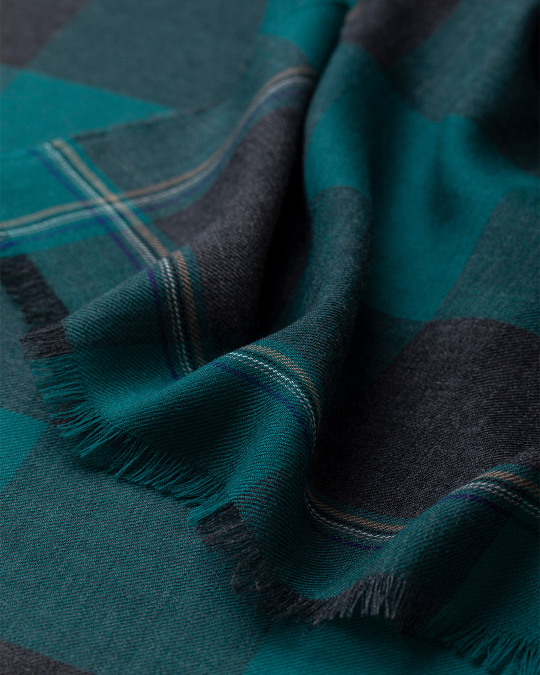 Close-up of a teal and navy plaid fabric with fringed edges. JOHNSTONS OF ELGIN CARNBEE LARGE GINGHAM SCARF GREEN 100% CASHMERE WA002476RU7709ONE