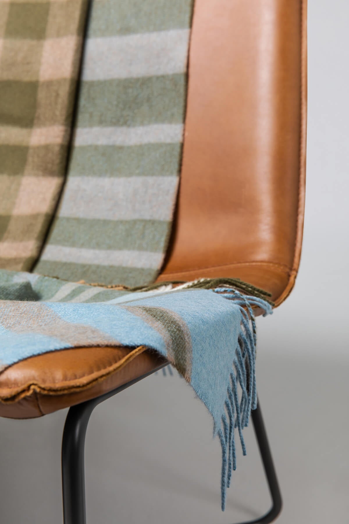 Johnstons of Elgin’s Anderson Modern Check Cashmere Throw on brown chair on a grey background WA000055RU7270ONE
