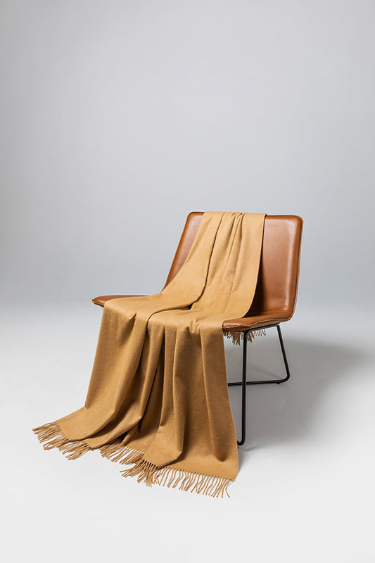 Johnstons of Elgin’s Camel Cashmere Throw on brown chair on a grey background WA000055SB4142