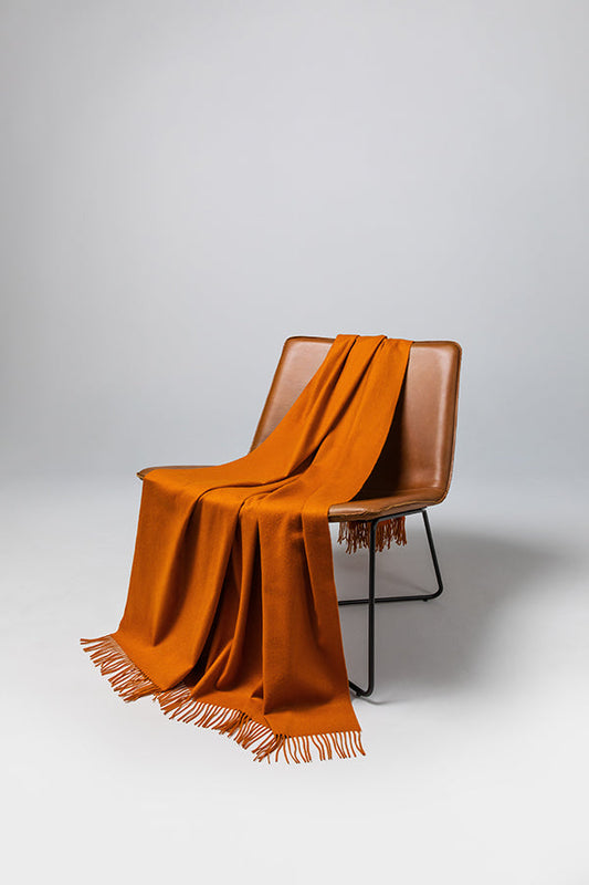 Johnstons of Elgin’s Ginger Cashmere Throw on brown chair on a grey background WA000055SG5046