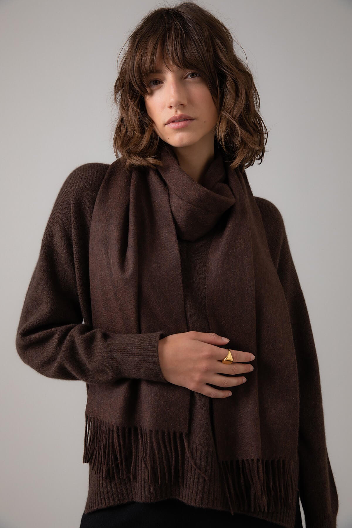 Model wearing Johnstons of Elgin Oversized Cashmere Scarf in Peat on a grey background WA000057HB7078ONE