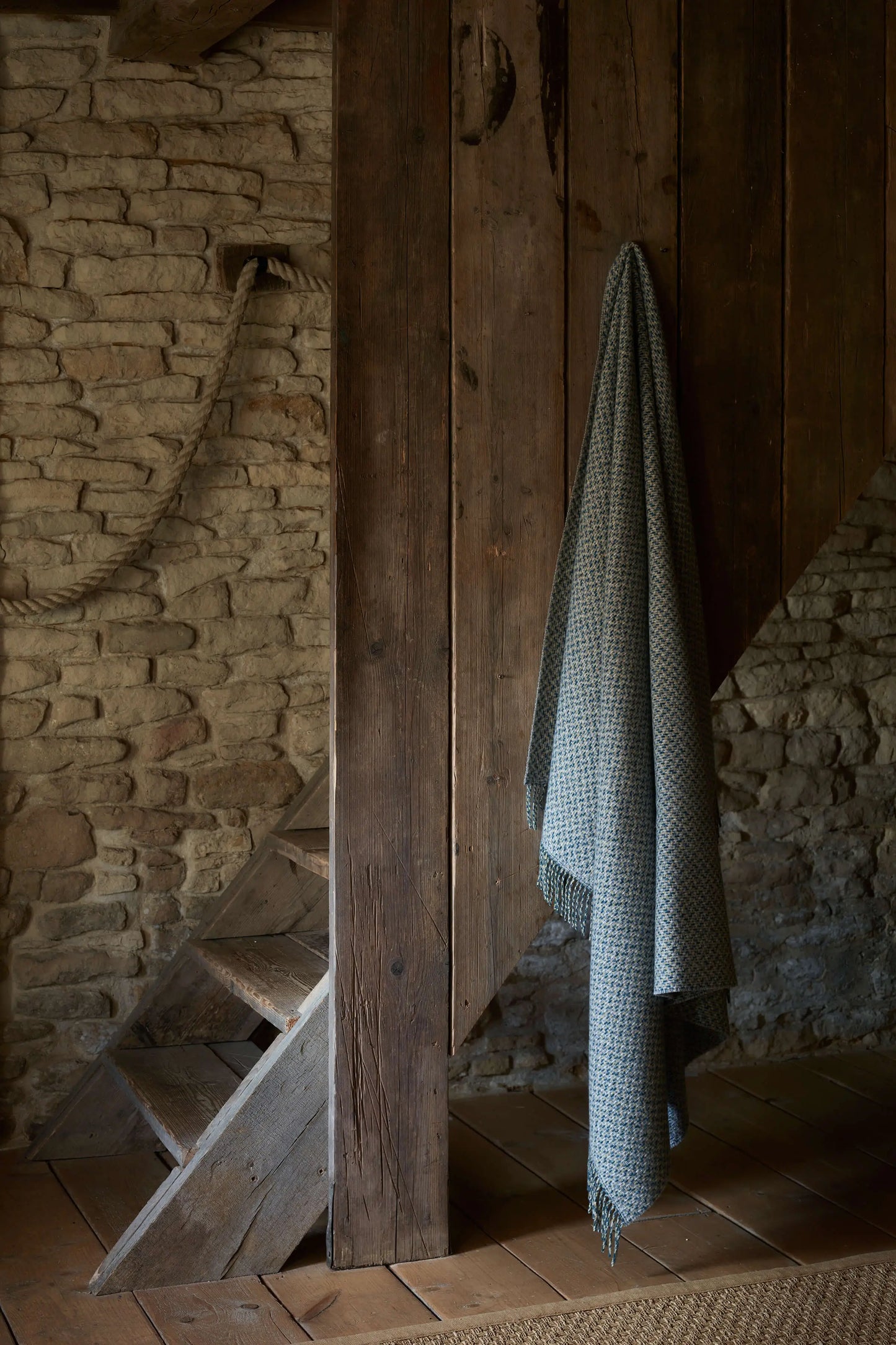 Johnstons of Elgin 2024 Blanket Collection Cool Neutral Tweed Texture Throw hanging on a wooden beam WB002458RU7549ONE