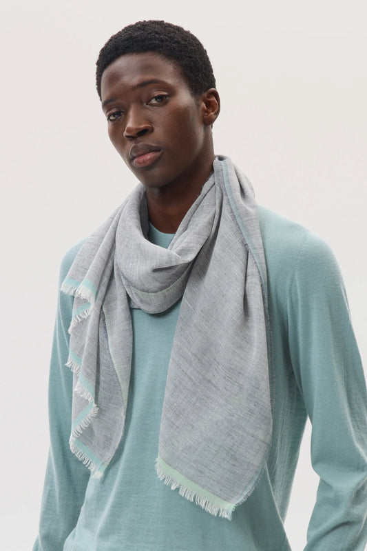 Male model wearing Johnstons of Elgin SS25 Accessories Grey Colour Border Lightweight Scarf layered over a cashmere jumper in jade green, on a white background WB002692RU7596ONE