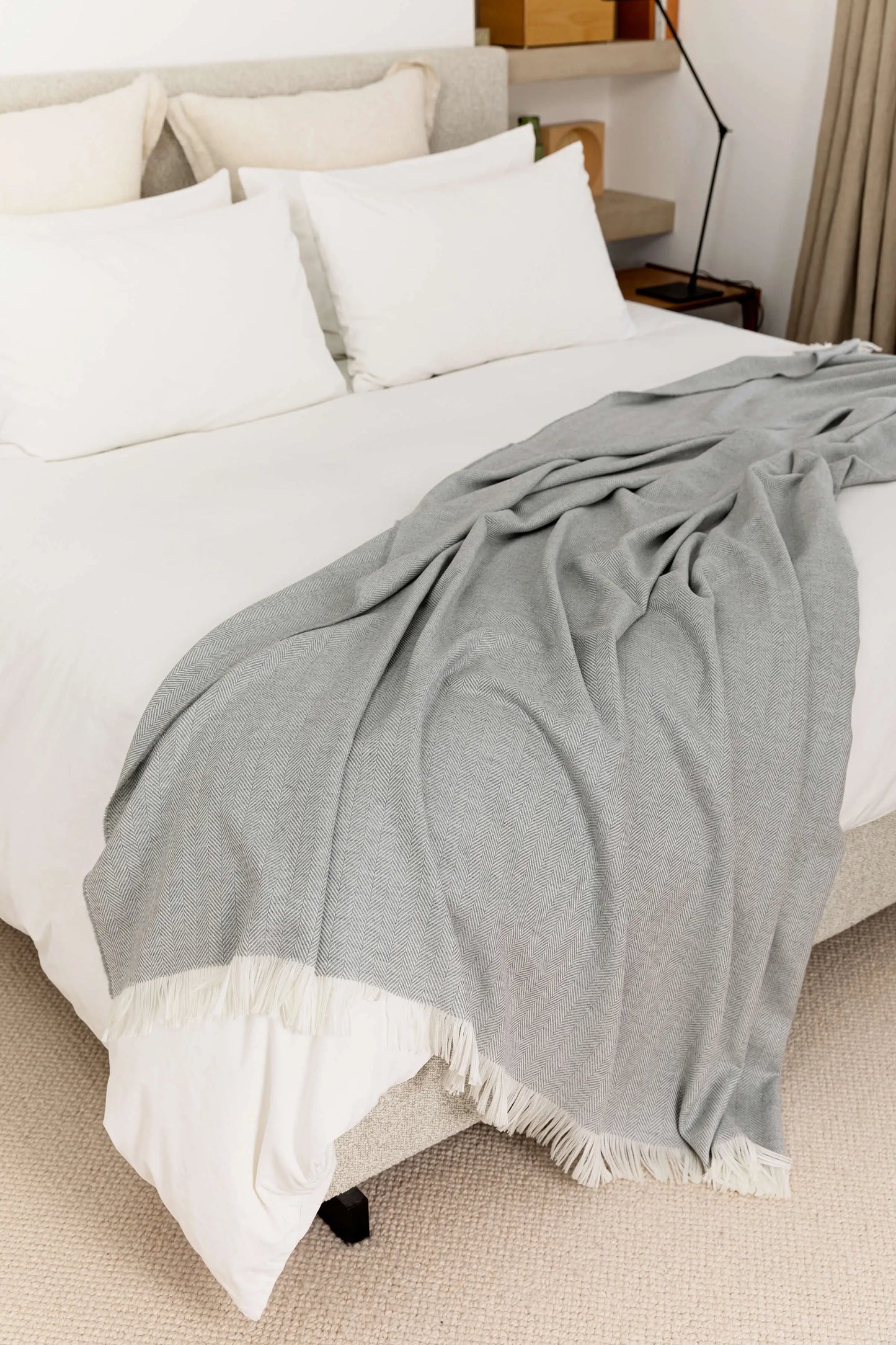 2025 Johnstons of Elgin Interiors Collection Mist & White Herringbone Merino Bed Throw draped on a white bed WD001115RU5857ONE