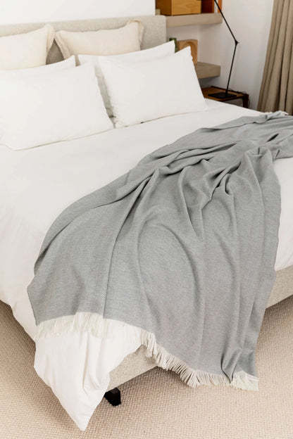 2025 Johnstons of Elgin Interiors Collection Mist & White Herringbone Merino Bed Throw draped on a white bed WD001115RU5857ONE