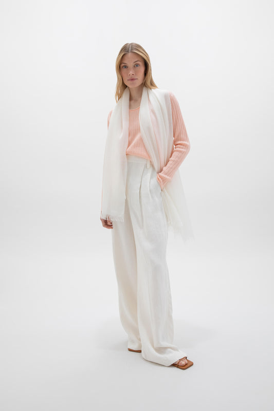 Johnstons of Elgin Lightweight Merino Wool Scarf in White worn by a female model over a peach cashmere sweater with white wide leg trousers shown on white background WD001093SA0000