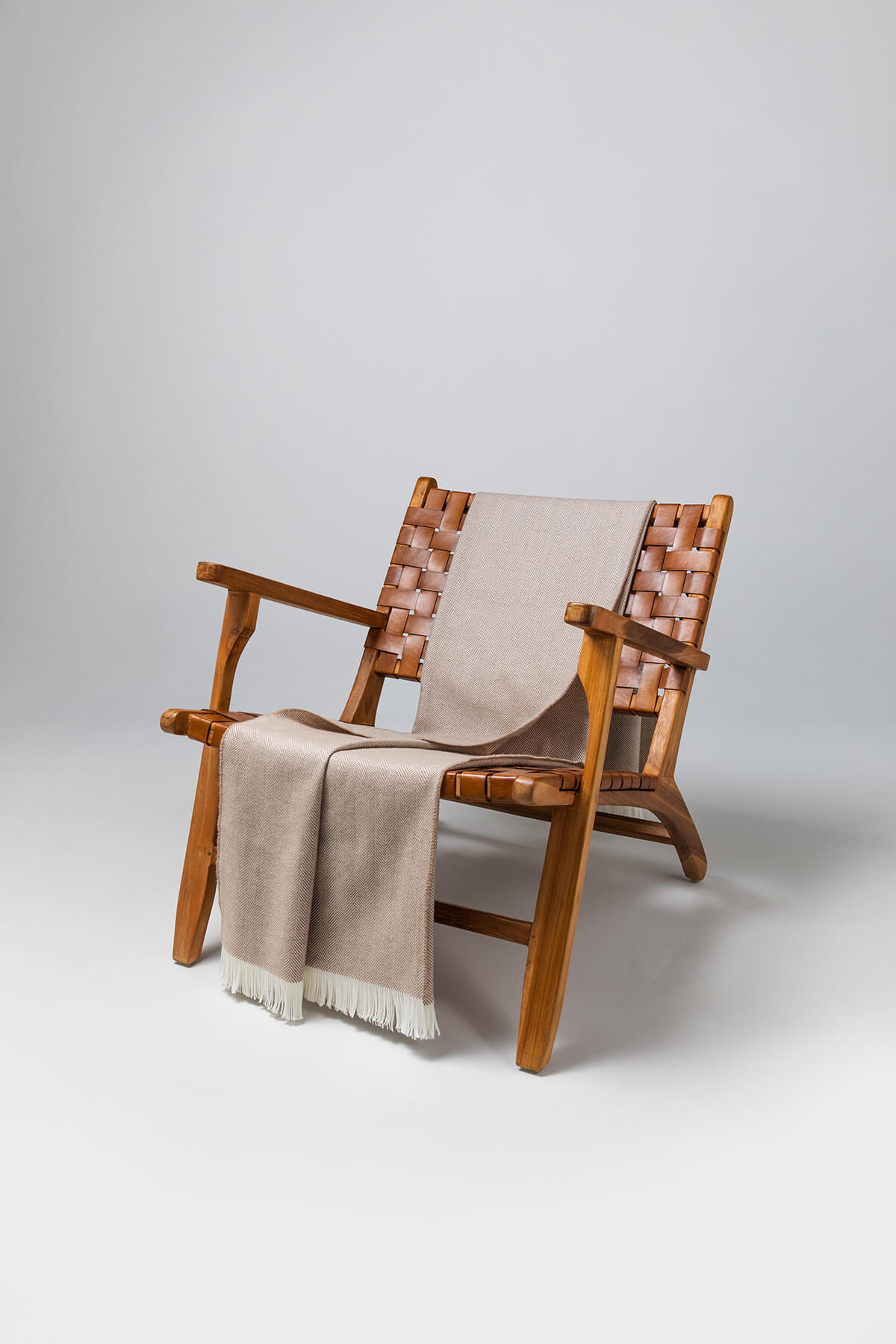 Johnstons of Elgin's Almond & White Herringbone Merino Throw on brown chair on a grey background WD000010RU5832ONE