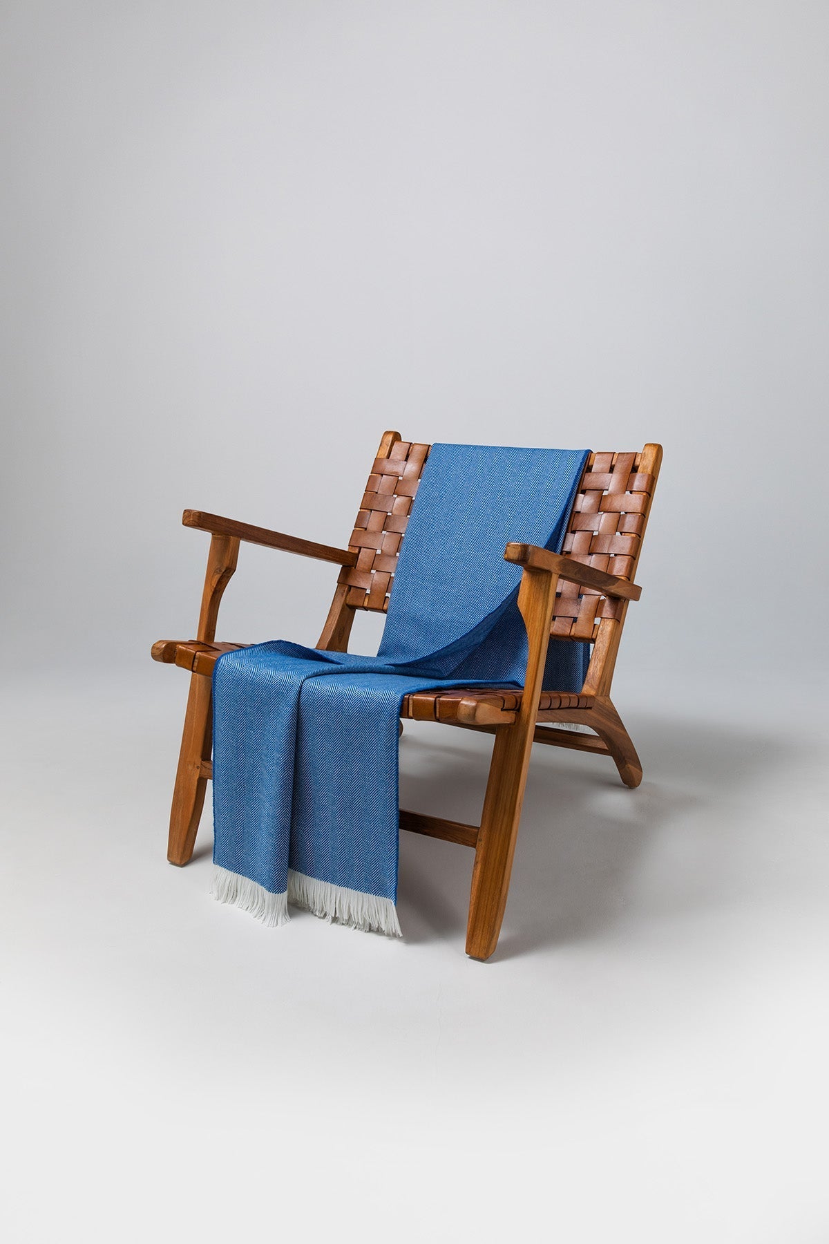 Johnstons of Elgin's Cobalt & White Herringbone Merino Throw on brown chair on a grey background WD000010RU7261ONE