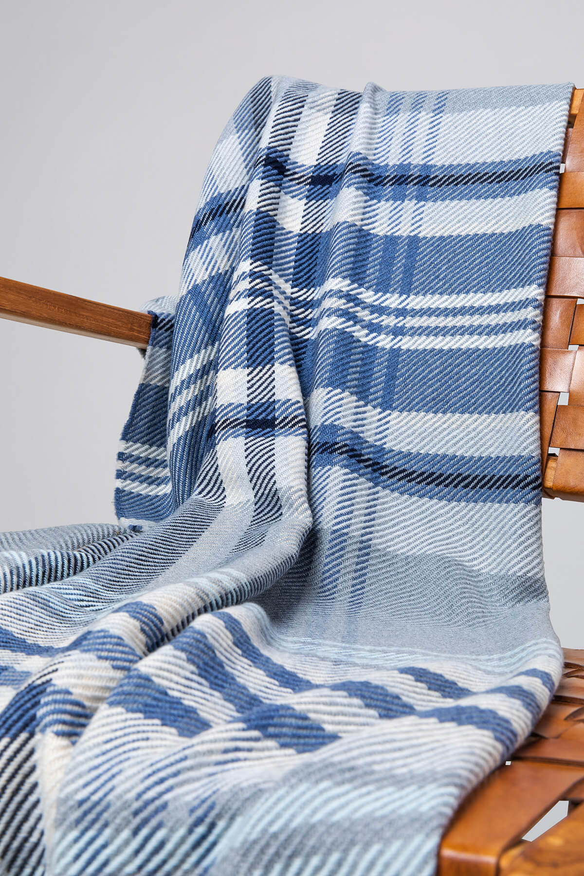 Johnstons of Elgin’s Blue & Grey Lofty Check Merino Throw on brown chair on a grey background WD001221RU6979ONE