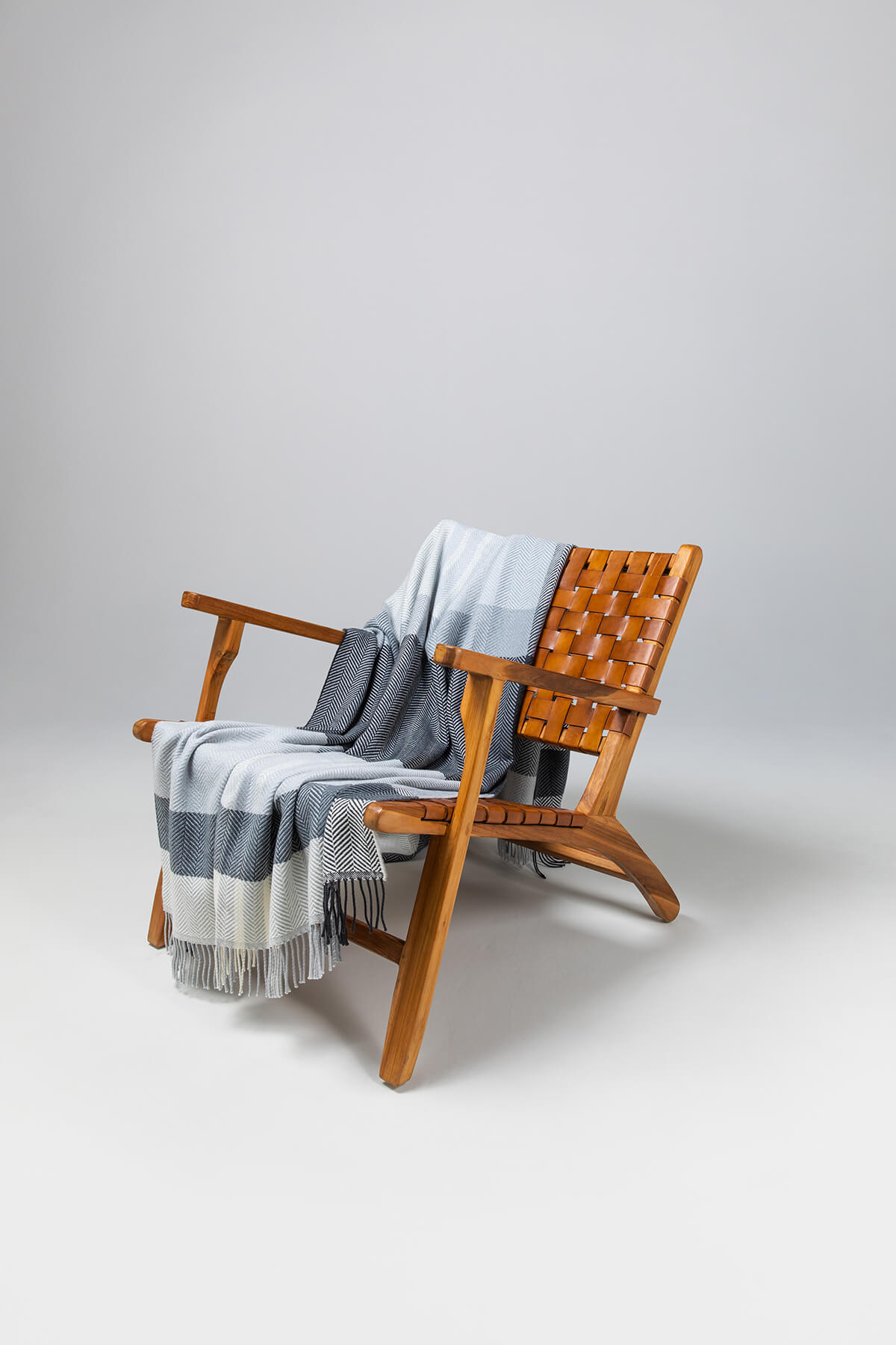 Johnstons of Elgin’s Grey & White Lofty Check Merino Throw on brown chair on a grey background WD001221RU6980ONE