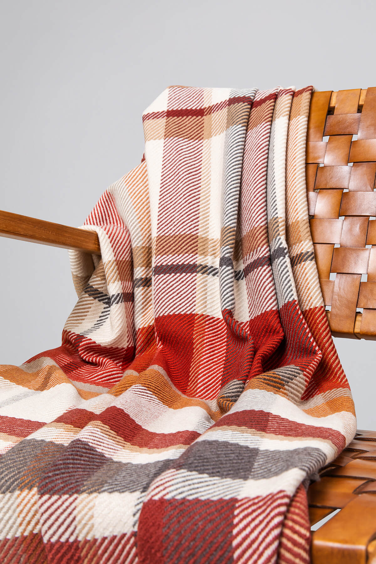 Johnstons of Elgin’s Auburn Red Lofty Check Merino Throw on brown chair on a grey background WD001221RU6981ONE