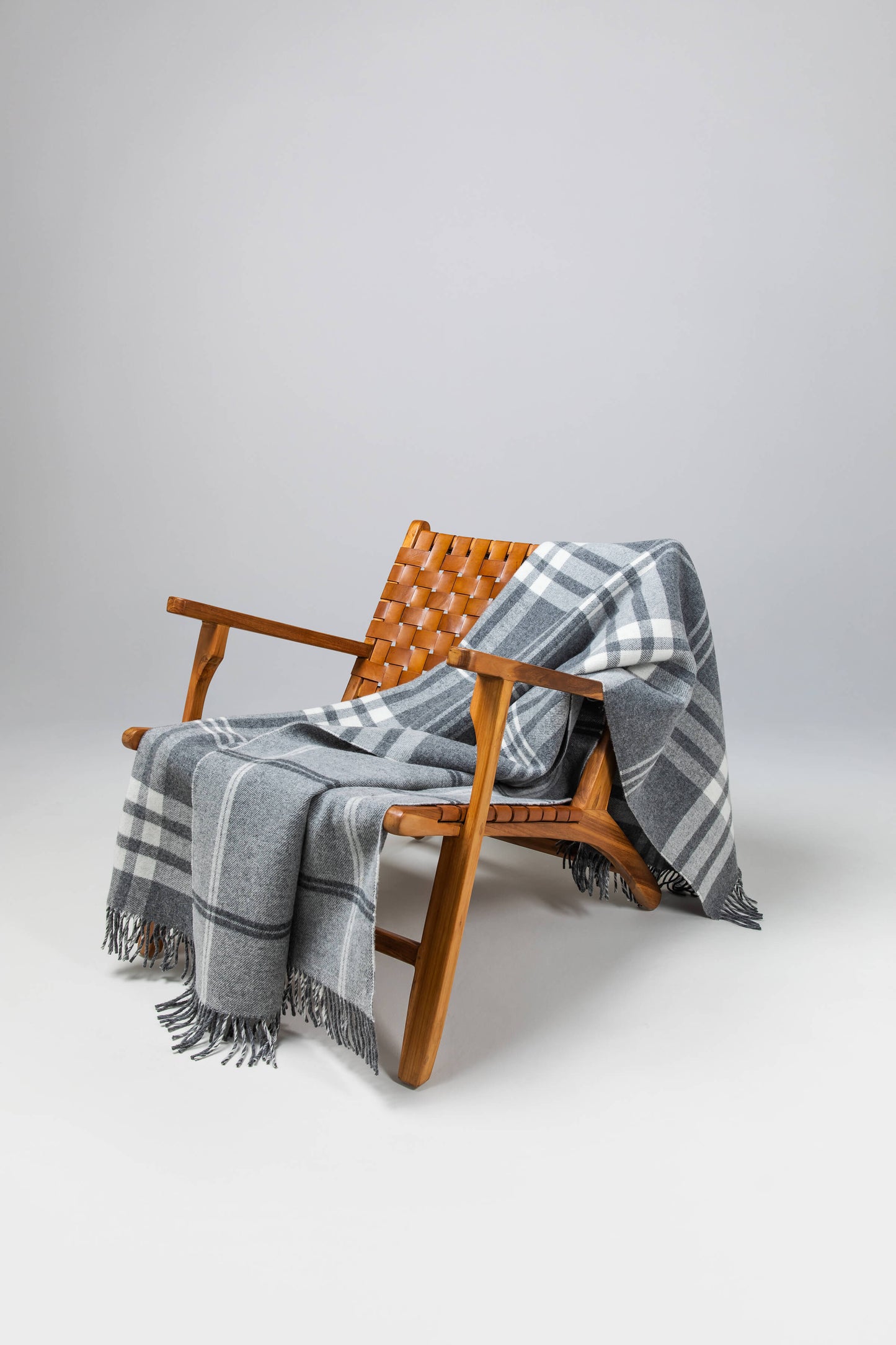 Johnstons of Elgin’s Double Face Grey & White Box Check Lambswool Throw on brown chair on a grey background WD000021RU6951ONE