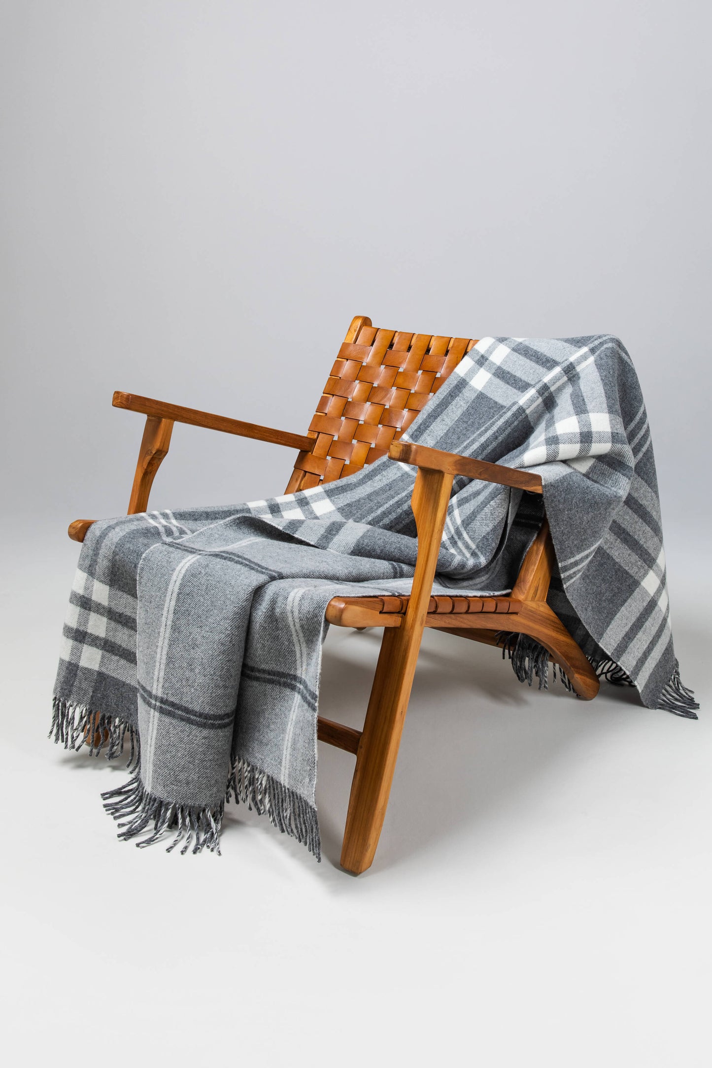 Johnstons of Elgin’s Double Face Grey & White Box Check Lambswool Throw on brown chair on a grey background WD000021RU6951ONE