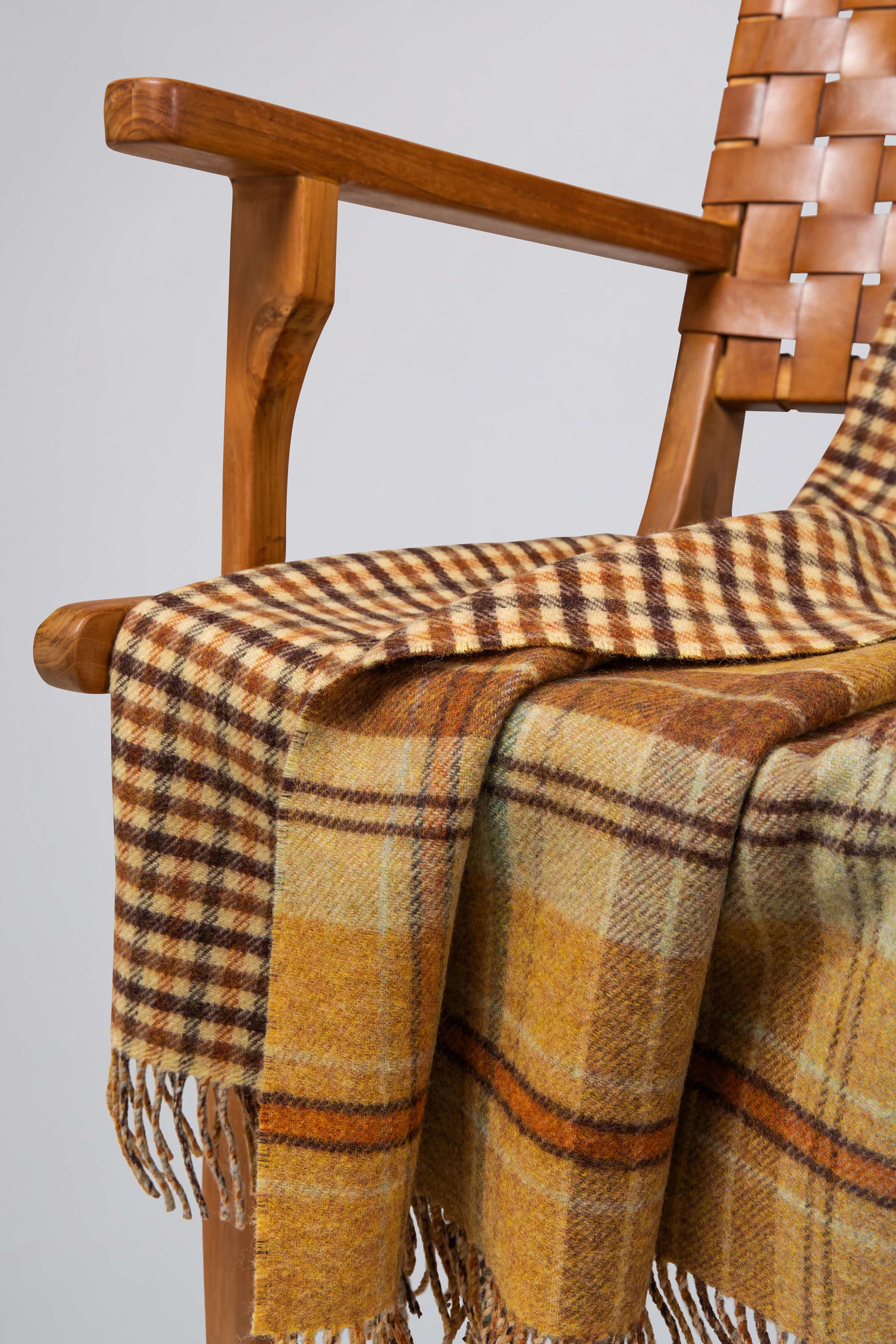 Johnstons of Elgin’s Double Face Findhorn Check Lambswool Throw on brown chair on a grey background WD000021XU0034N/A