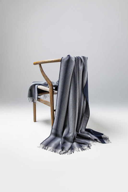 Johnstons of Elgin’s Ombre White & Navy Stripe Merino Throw on brown chair on a grey background WD000257RU6989ONE
