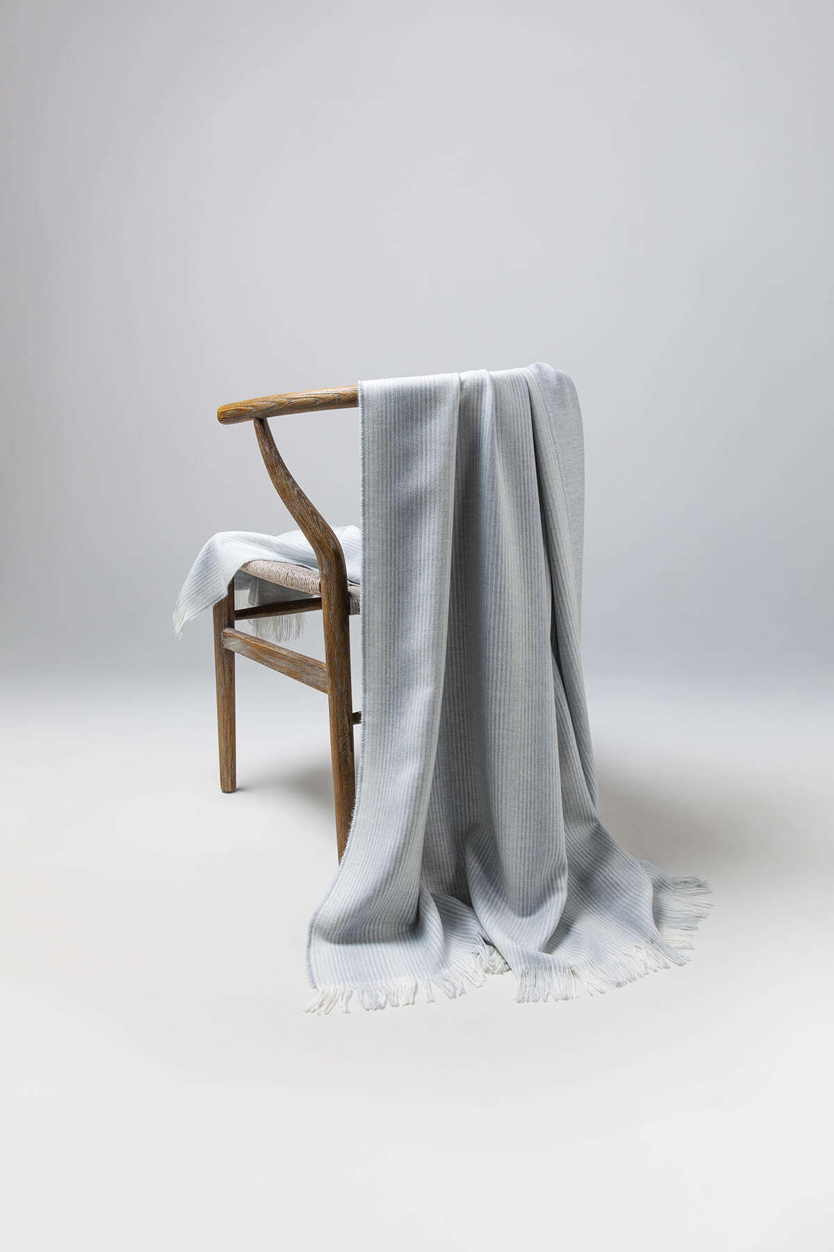 Johnstons of Elgin’s Silver & White Ombre Stripe Merino Throw on brown chair on a grey background WD000257RU6990ONE