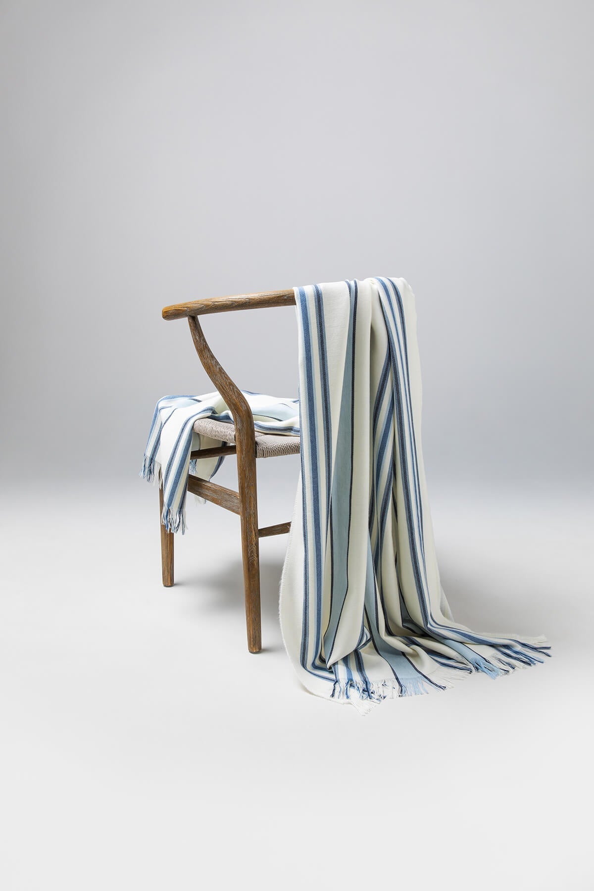 Johnstons of Elgin’s Simple Blue Stripe Merino Throw on brown chair on a grey background WD000257RU6991ONE