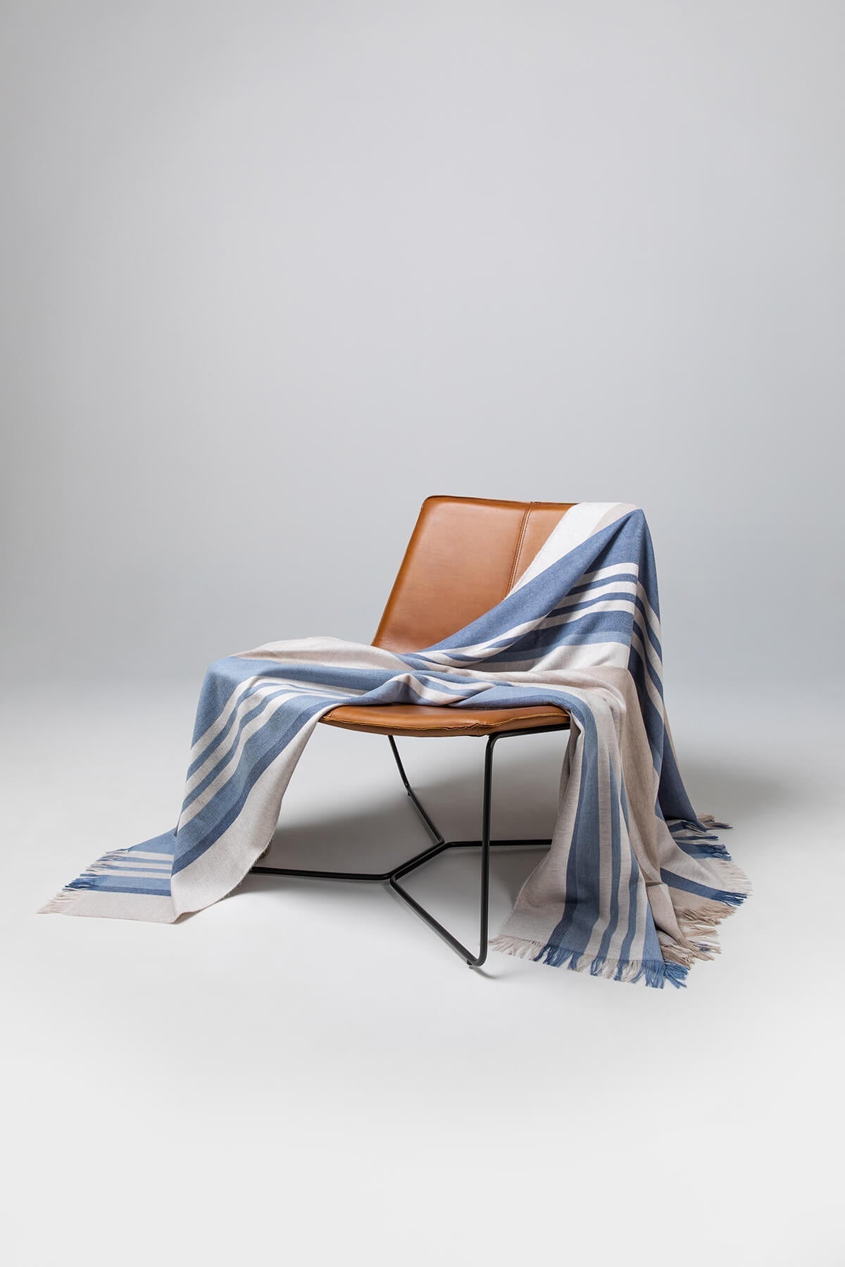 Johnstons of Elgin’s Bold Stripe Blue Merino Throw on brown chair on a grey background WD000257RU6993ONE