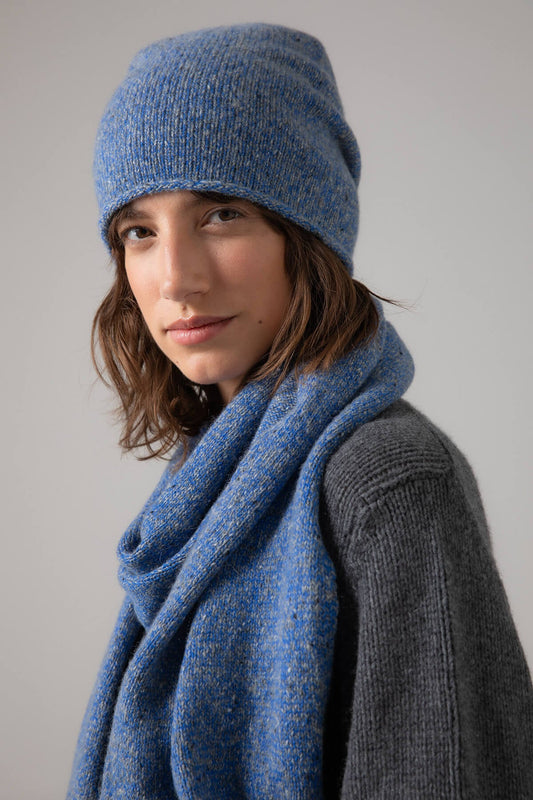 Johnstons of Elgin’s Donegal Cashmere Beanie and Scarf Giftset in Orkney Blue on a model wearing a grey cashmere jumper on a grey background AW23GIFTSET3B
