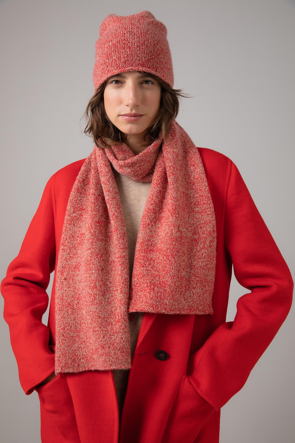 Johnstons of Elgin’s Orkney Red Camel Cashmere Donegal Marl Beanie on model wearing matching cashmere red scarf with red coat on a grey background  HAY03303004530